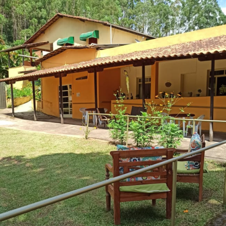 Jardim do Residencial Recanto Verde com duas poltronas na grana e casa amarela ao fundo