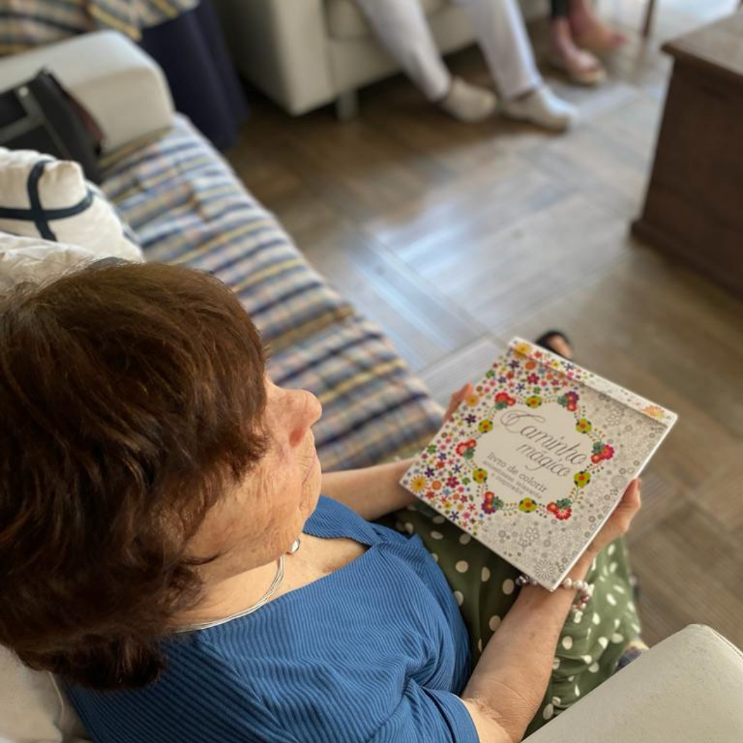 Senhora sentada no sofá com livro de colorir nas mãos