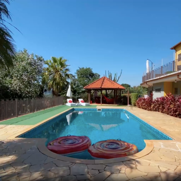 Vista da piscina da Estância das Flores com a casa ao fundo e varanda.