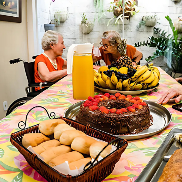 Incentivo ao convívio comunitário ao redor de uma mesa decorada com frutas, bolo e pães frescos, simbolizando momentos de convivência e afeto.