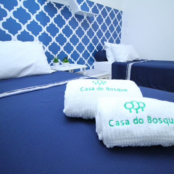 Quarto com duas camas e bonita decoração em tons de azul escuro, com toalhas bordadas sobre a cama