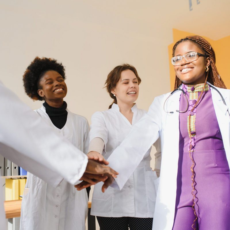 Mature doctors and young nurses stacking hands together at hospital. Close up hands of medical team stacking hands. Group of successful medical doctors and nurses stack of hands.